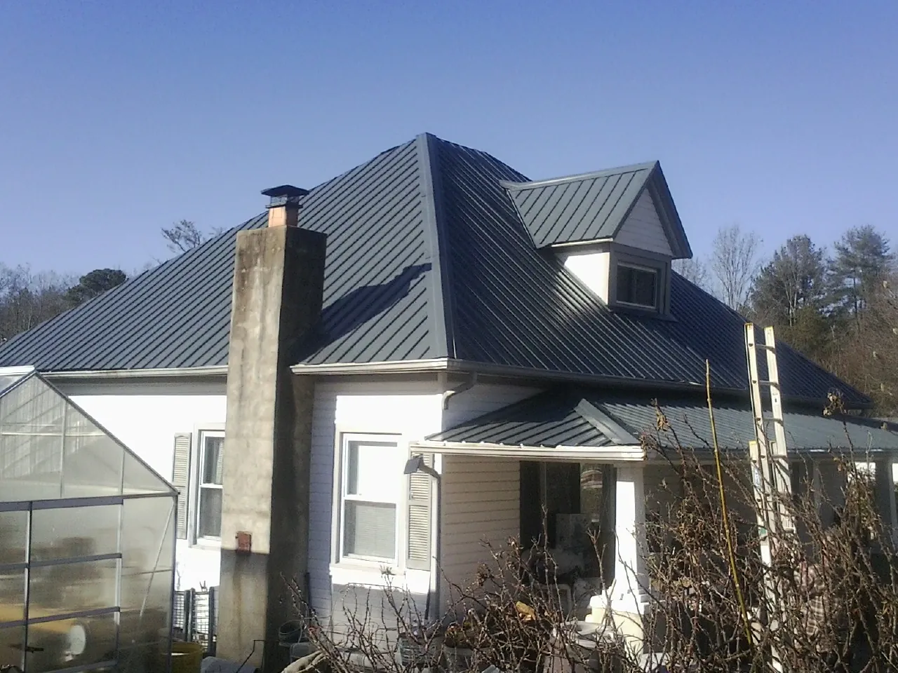 Dark blue standing seam metal roof on a white farmhouse with dormer in North Hollywood