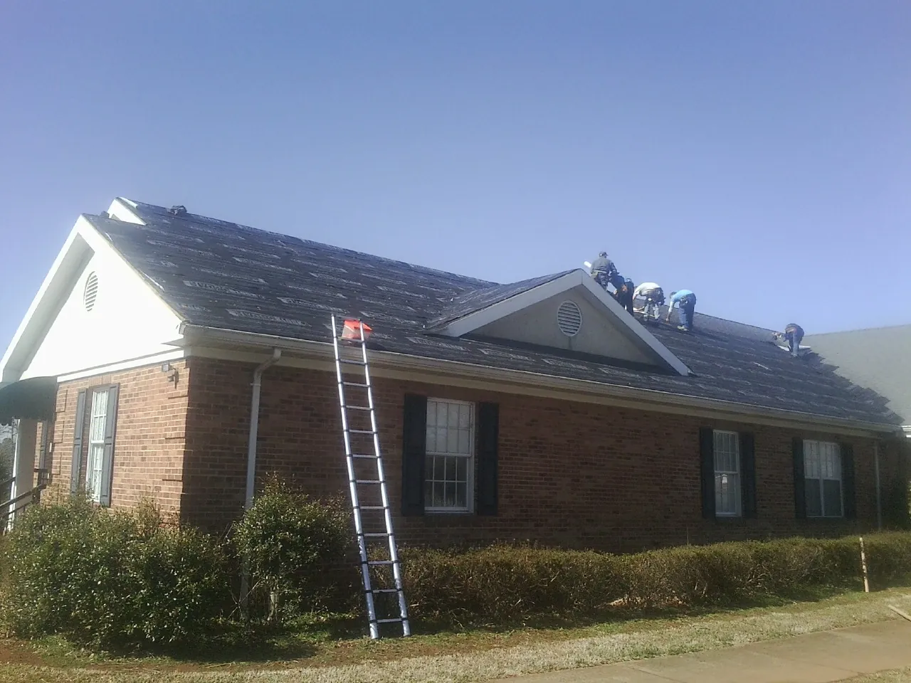 Crew tearing shingles off a brick ranch roof with a ladder set — Emergency Roof Repair work by our crew in North Hollywood