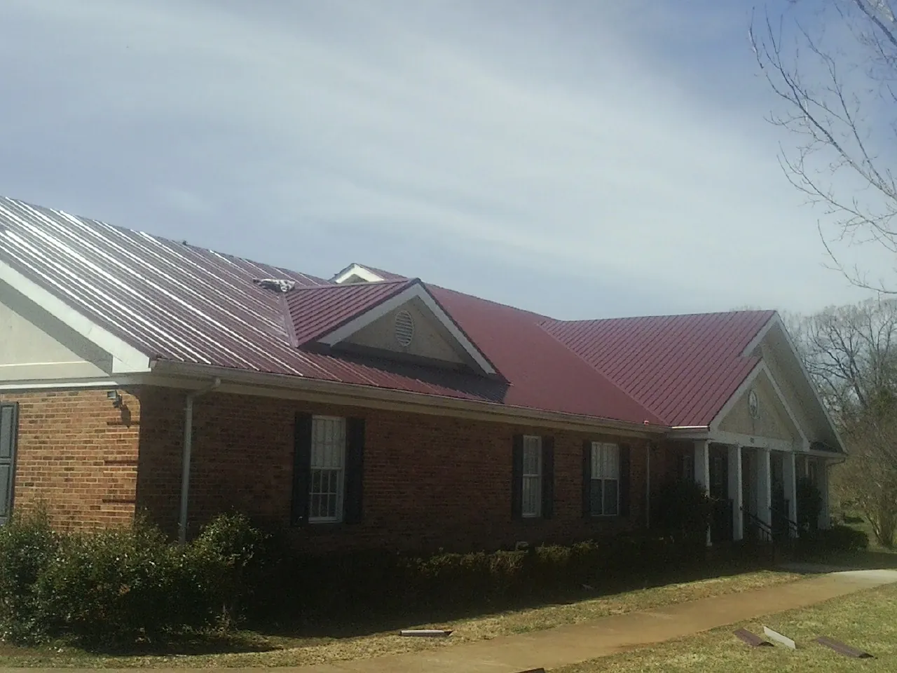 Red metal roof with gabled entries on a long brick building, from a Hail Damage Roof Repair job in North Hollywood