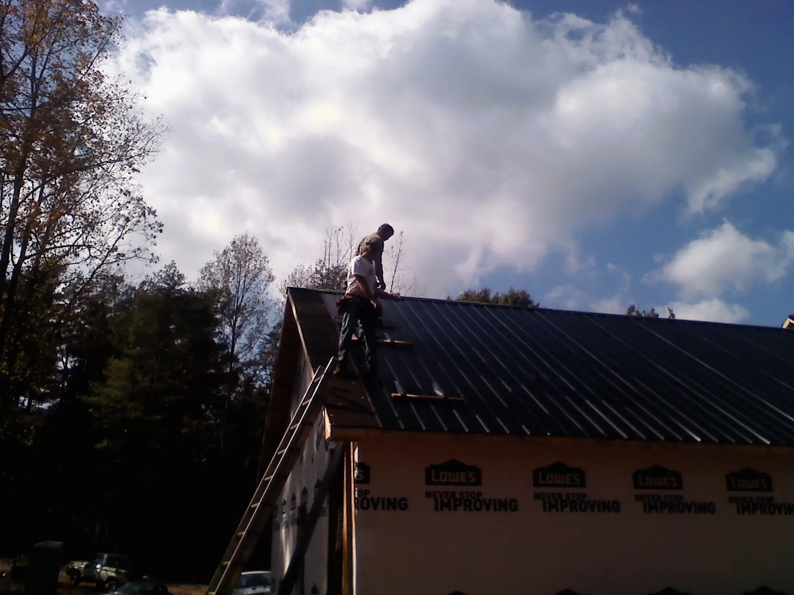Roofer fastening dark metal panels high against a cloudy sky, from a Roof Inspection job in North Hollywood