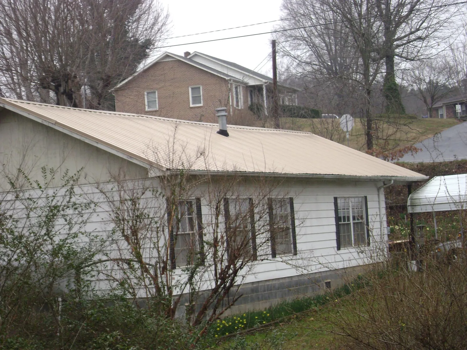 Tan metal roof on a white sided house set into a hillside — Commercial Roofing by Roofing Brothers in North Hollywood